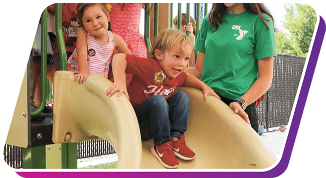 Two children playing on a slide being supervised by YMCA staff